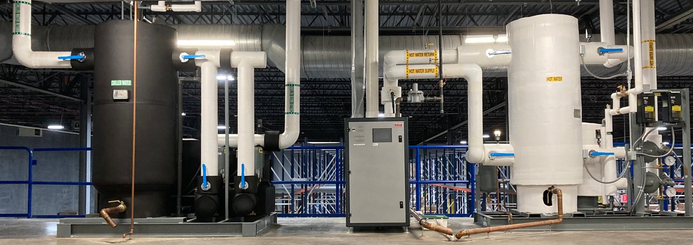 Hot water tanks, piping, and control panel in a plant mechanical room